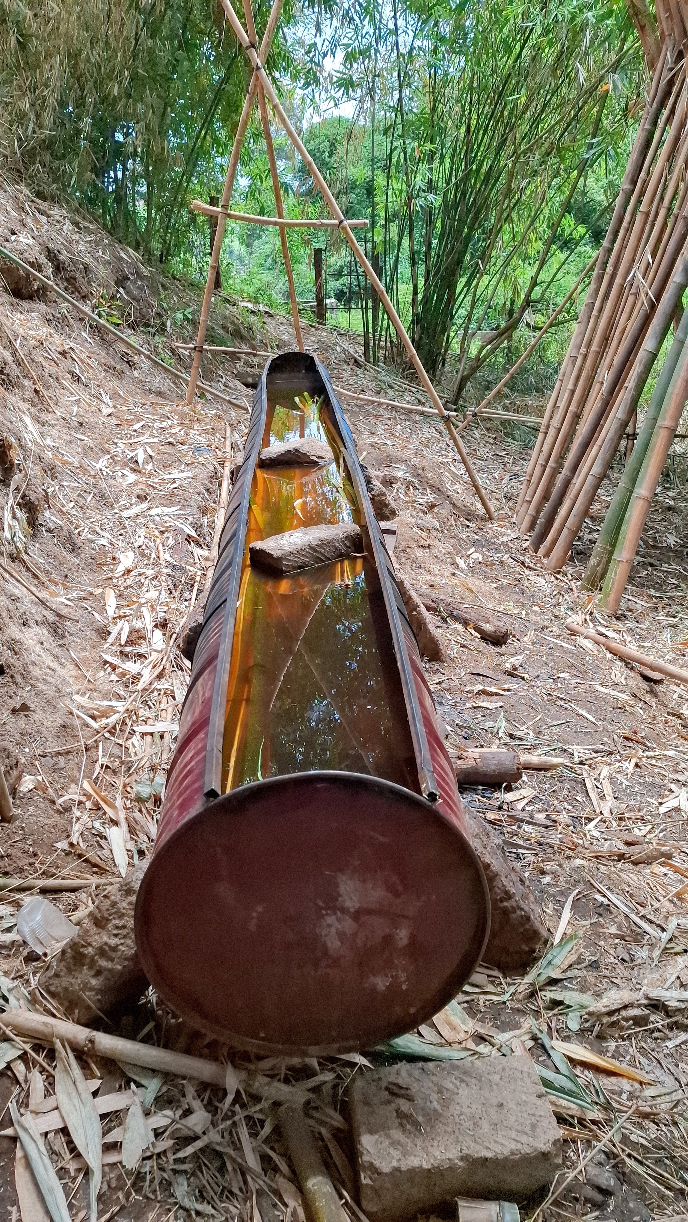 44 gallon drums welded together on their side creating a container which contains bamboos and treatment solution with cement bricks placed on top to weigh down the bamboo so it remains submerged in the borax solution